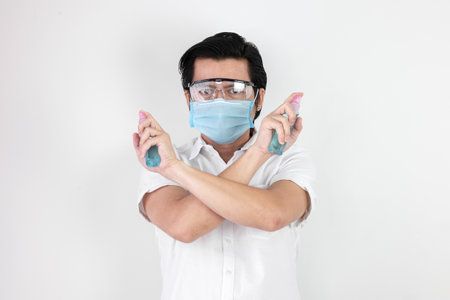 Asian man on a white background are strengthening to overcome the virus by wearing a mask and carrying alcohol bottles for washing hands, cleaning or spraying infected items. Covid-19 conceptの写真素材