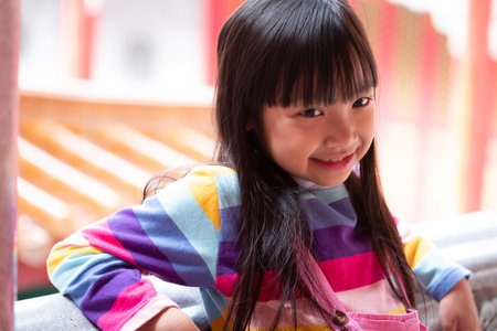 Asian child girl wearing jumpsuit jeans and T-shirts of many colors sitting on the balcony and smile...