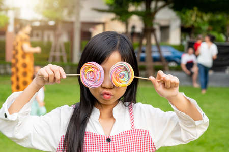 Asian child girl holds a rainbow meringue to cover her eyes humorously.の写真素材