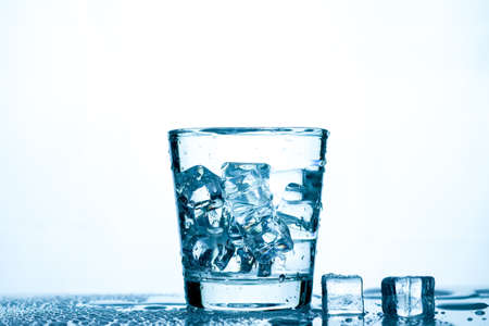 drinking water into a clear glass with ice on the table on a white background with copy space.の写真素材