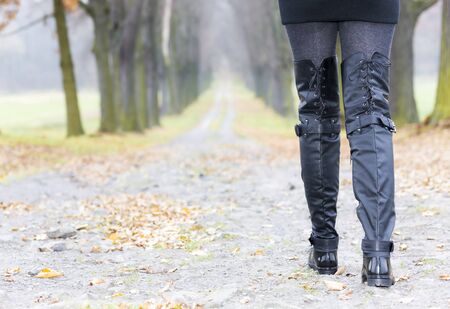detail of woman wearing black clothes and boots in autumnal alley