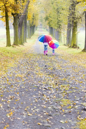 mother and her daughter with umbrellas in autumnal alleyの写真素材