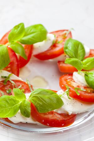 Delicious caprese salad with ripe tomatoes and mozzarella cheese with fresh basil leaves. Italian...