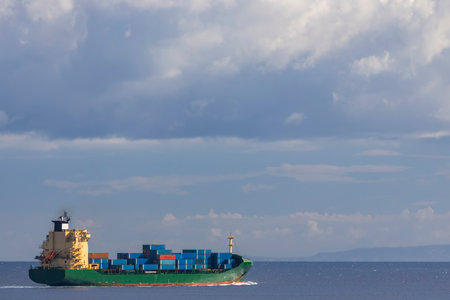 cargo ship nearby Capo Peloro Lighthouse in Punta del Faro on the Strait of Messina, most north...