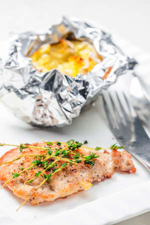 chicken steak with baked potato in aluminum foilの写真素材