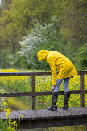 Young woman with yellow raincoat and rubber boots in spring natureの写真素材