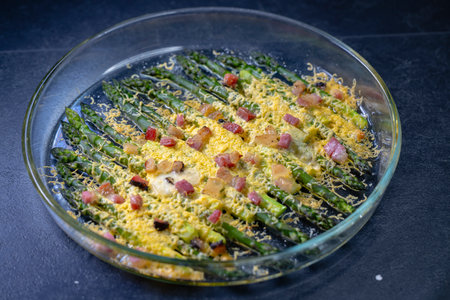 Green asparagus baked in cheddar with bacon cubeson on black backgroundの写真素材