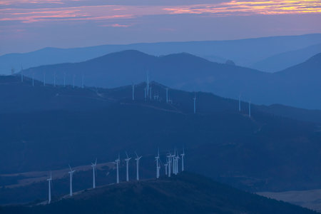 Wind farm generating renewable energy during a beautiful sunset over a mountain range
