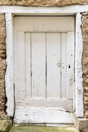 White weathered wooden door with peeling paint and rusty metal hardware, set in a stone wall in Saint Hilaire, Franceの写真素材
