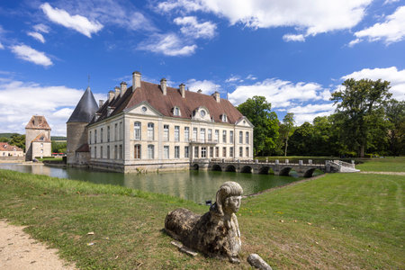 Scenic view of the historic Chateau de Commarin in Burgundy, France, reflecting in the water of its moat, with a sphinx statue in the foregroundの写真素材
