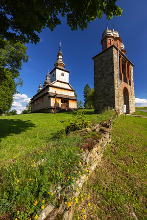 View of the wooden Church of Saint Michael the Archangel and its bell tower in Brunary, Poland, standing on a green hill under blue skyの写真素材