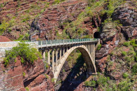 Concrete bridge crossing a canyon with red rocks and leading to a tunnel in Guillaumes, Provence Alpes Cote d'Azur, Franceの写真素材