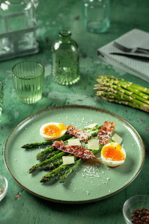Delicious and healthy green asparagus salad with bacon, parmesan and soft boiled eggs served on a green plateの写真素材