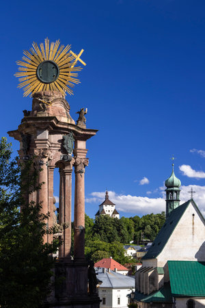 Holy Trinity column with golden sun and cross dominating the skyline of Banska Stiavnica, including the Old Castle and a church, in Slovakiaの写真素材