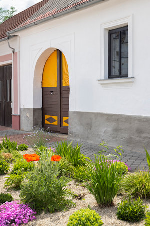 Charming facade of a traditional house with a colorful arched wooden door and a vibrant flower garden in Stare Mesto pod Landstejnem, Czech Republicの写真素材