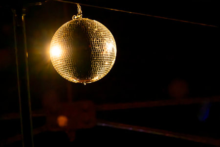 Shiny disco ball hanging from the ceiling, reflecting golden light in a dark nightclub, creating a festive atmosphereの写真素材