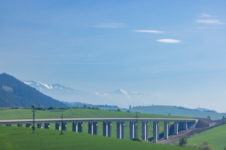Long highway viaduct crossing green fields in Likavka, Slovakia, with the majestic Tatra Mountains visible in the background, a beautiful spring landscapeの写真素材