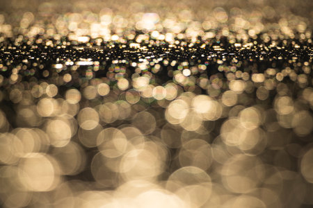 Golden bokeh reflecting on water surface creating a beautiful abstract background, perfect for luxury, festive or christmas themesの写真素材