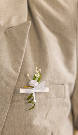 Elegant boutonniere with white rose and ribbon pinned to groom's light gray suit lapel, adding a...