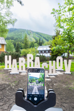 Smartphone on tripod capturing Harrachov sign with mountain in background in Liberecky kraj, Czechia