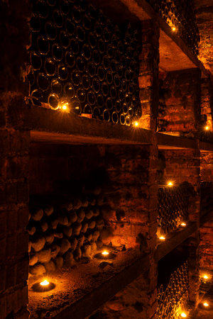 Dusty wine bottles resting in a dark cellar with warm candlelight, creating an evocative atmosphereの写真素材