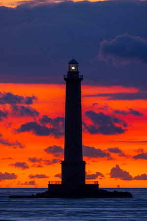 Silhouette of Phare de la Hague lighthouse against a vibrant sunset sky in Normandy, Franceの写真素材
