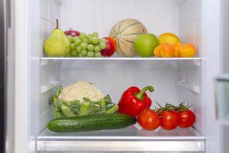 Fresh produce, including fruits and vegetables, neatly arranged on shelves inside an open refrigerator, promoting a healthy lifestyleの写真素材