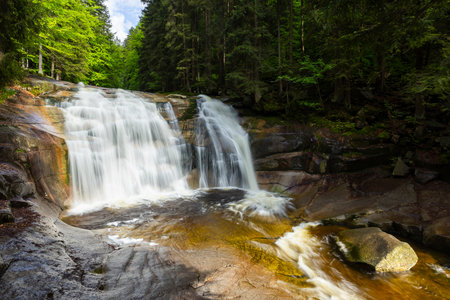 Scenic view of Mumlava Waterfall flowing over rocks in a tranquil forest setting in Harrachov, Czechiaの写真素材