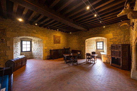 Interior of a medieval castle room showing wooden furniture, terracotta floor, stone walls, and exposed wooden beamsの写真素材
