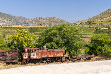 Old rusty abandoned steam train in Vila Nova de Foz Coa, Portugal, with vineyards and electrical substation in the backgroundの写真素材