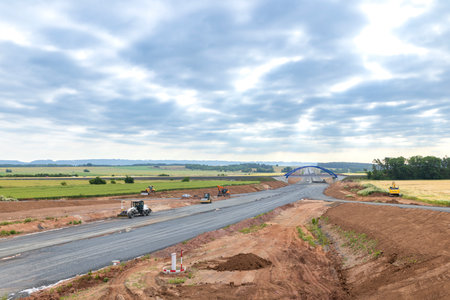 Heavy machinery paving a new road under a cloudy skyの写真素材