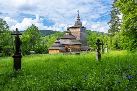 Wooden church in Sekowa, Poland, surrounded by lush greenery and a serene cemetery, showcasing traditional architectureの写真素材