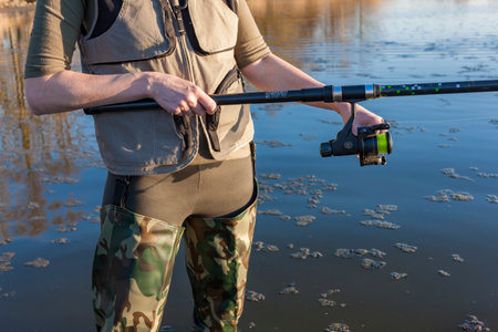 Fisher holding fishing rod wearing camouflage waders and fishing vestの写真素材