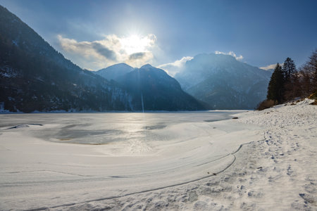 Serene winter scene of a frozen lake surrounded by mountains in Tarvisio, Italyの写真素材