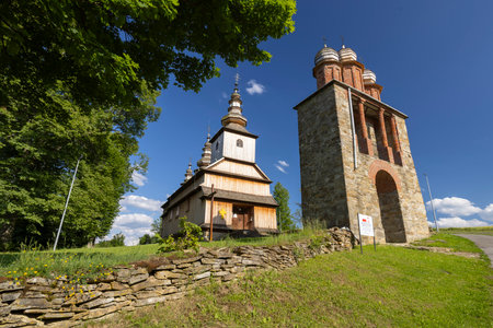 Traditional wooden church beside a tall stone bell tower under a clear blue skyの写真素材