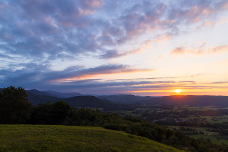 Vibrant sunset casting colorful hues over lush green landscapeの写真素材