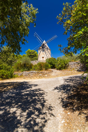 Scenic windmill stands amidst trees under a clear blue skyの写真素材