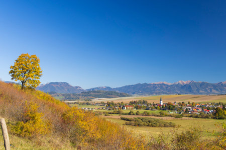Picturesque village in Slovakia surrounded by autumn foliage and distant mountainsの写真素材