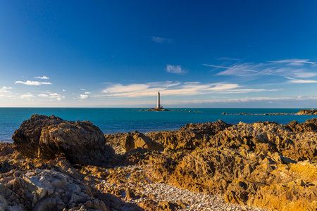 Lighthouse on rocky shore under clear blue sky in La Hague, Franceの写真素材