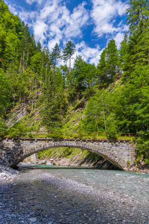 Scenic view of an old stone bridge over a clear river flowing through a lush green forest in Bregenzerwald, Vorarlberg, Austriaの写真素材