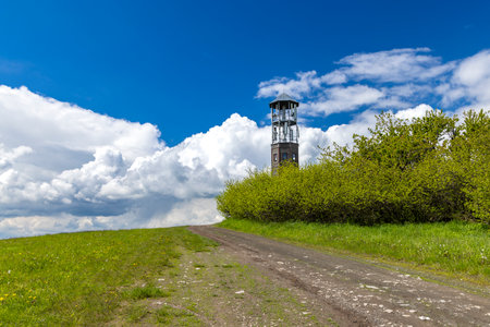 Observation tower rising above green hill in Nackovice, Loveckovice, Czechia, with cloudy sky in backgroundの写真素材