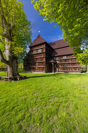 The UNESCO protected articular wooden church of Hronsek basks in spring sunlight, surrounded by lush greenery and a clear blue skyの写真素材