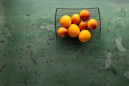 Lemons and oranges arranged in a black wire basket on a textured green surfaceの写真素材