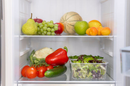 Assorted produce neatly arranged on refrigerator shelvesの写真素材