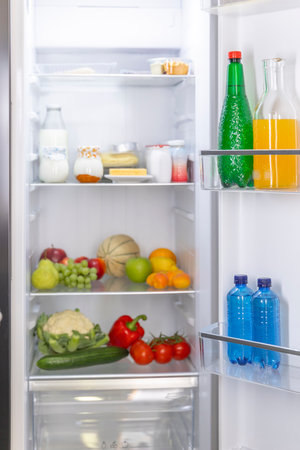 Open fridge showcasing fruits, vegetables, and beverages neatly arrangedの写真素材