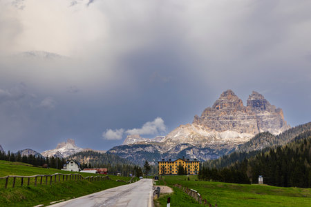 Empty road leading to a hotel in Auronzo di Cadore, with the Tre Cime di Lavaredo towering in the background under a dramatic skyの写真素材
