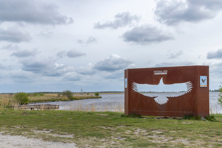 Rusty metal entrance sign of Lauwersmeer National Park with white tailed eagle shape and lake on backgroundの写真素材