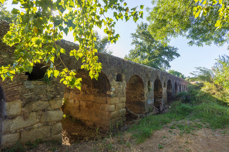 Sunlight filters through the arches of an ancient Roman bridge, highlighting its historical significance in Cuba, Beja, Portugalの写真素材