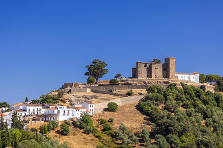 Medieval fortress Cortegana Castle standing tall on a hill above white houses of Cortegana village under clear blue sky in Huelva, Andalucia, Spainの写真素材
