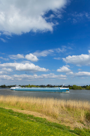 Blue barge sailing on the Lek river in Lopik, Utrecht, Netherlands, on a sunny day with beautiful cloudsの写真素材